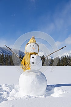 Cute fun snowman with knit hat and scarf in winter landscape snow scene with mountains and blue sky