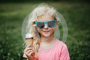 Cute funny adorable girl in sunglasses with dirty nose and moustaches eating ice cream from waffle cone. Happy cool hipster child