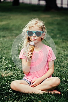 Cute funny adorable girl in sunglasses with dirty nose and moustaches eating ice cream from waffle cone. Happy cool hipster child