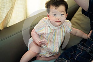 Cute funny Asian toddler baby girl smiles and looking up while playing next to mother on sofa at home.Nursery  and baby