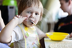 Cute funny baby boy 2 years old sitting with a spoon in his mouth and looking at the camera, baby food concept