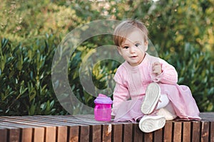 Cute funny baby girl 1 year old wear pink dress sitting with plastic bottle with water