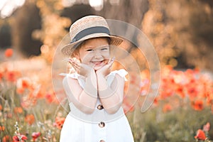 Cute funny baby girl 2-3 year old wear straw hat and white summer dress over flower meadow background. Kid laughing outdoors over