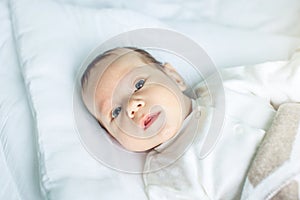 Cute funny baby lying on a white bed covered with a blanket. Concept of The tenderness of motherhood and family values