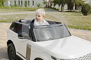 blond little young toddler kid child boy sitting,driving,riding in electric toy car,automobile,jeep in park.Children