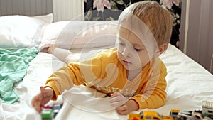 Cute funny boy with dirty face lying on bed and playing with colorful cars. Child development, education.