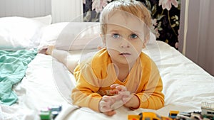 Cute funny boy with dirty face lying on bed and playing with colorful cars. Child development, education and entertainment