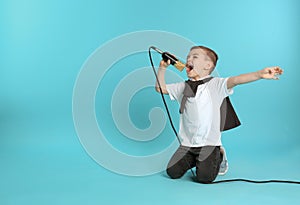 Cute funny boy with microphone on color background.