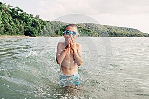 Cute funny Caucasian boy swimming in lake river with underwater goggles. Child diving in water