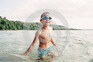 Cute funny Caucasian boy swimming in lake river with underwater goggles. Child diving in water