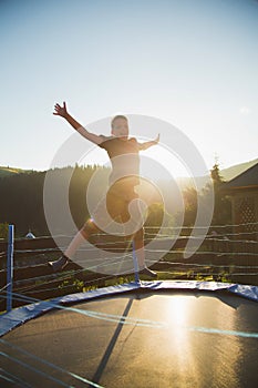 Cute funny cheerful young kid jumping outdoors at trampoline