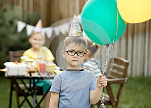 Cute funny four year old boy celebrating his birthday with family or friends in a backyard. Birthday party. Kid wearing