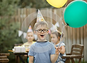 Cute funny four year old boy celebrating his birthday with family or friends in a backyard. Birthday party. Kid wearing