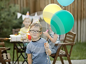 Cute funny four year old boy celebrating his birthday with family or friends in a backyard. Birthday party. Kid wearing