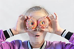 A cute funny girl in a blue t-shirt holds bright pink donuts near her eyes like glasses and looks at you on a pink