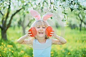 Cute funny girl with Easter eggs and bunny ears at garden. easter concept. Laughing child at Easter egg hunt