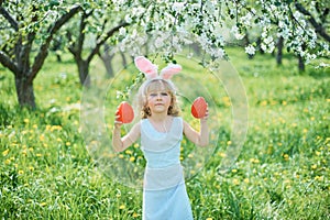 Cute funny girl with Easter eggs and bunny ears at garden. easter concept. Laughing child at Easter egg hunt