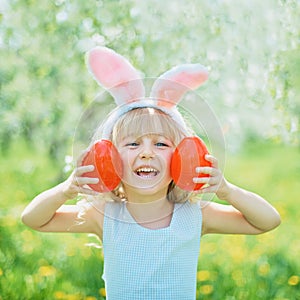 Cute funny girl with Easter eggs and bunny ears at garden. easter concept. Laughing child at Easter egg hunt