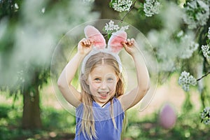 Cute funny girl with Easter eggs and bunny ears at garden. easter concept. Laughing child at Easter egg hunt