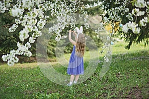 Cute funny girl with Easter eggs and bunny ears at garden. easter concept. Laughing child at Easter egg hunt