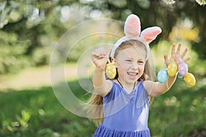 Cute funny girl with Easter eggs and bunny ears at garden. easter concept. Laughing child at Easter egg hunt