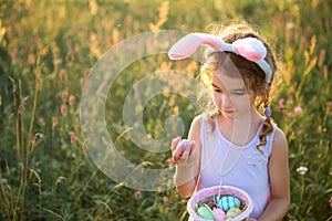 Cute funny girl with painted Easter eggs in spring in nature in a field with golden sunlight and flowers. Easter holiday, Easter