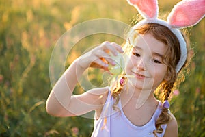 Cute funny girl with painted Easter eggs in spring in nature in a field with golden sunlight and flowers. Easter holiday, Easter