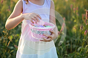 Cute funny girl with painted Easter eggs in spring in nature in a field with golden sunlight and flowers. Easter holiday, Easter