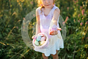 Cute funny girl with painted Easter eggs in spring in nature in a field with golden sunlight and flowers. Easter holiday, Easter