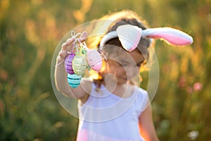 Cute funny girl with painted Easter eggs in spring in nature in a field with golden sunlight and flowers. Easter holiday, Easter