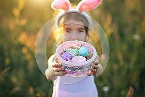 Cute funny girl with painted Easter eggs in spring in nature in a field with golden sunlight and flowers. Easter holiday, Easter
