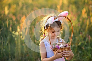 Cute funny girl with painted Easter eggs in spring in nature in a field with golden sunlight and flowers. Easter holiday, Easter