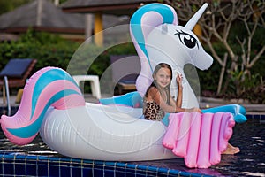 Cute funny girl sitting chilling on inflatable ring unicorn. Kid child enjoying having fun in swimming pool. Summer outdoor water