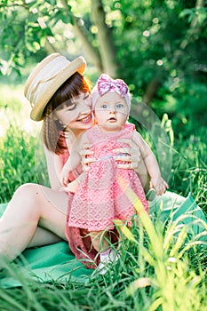 Cute funny happy baby making his first steps on a green grass, mother holding her hands supporting by learning to walk