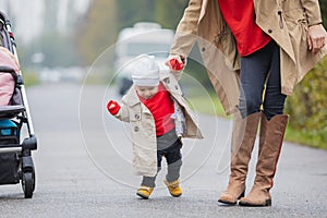 Cute funny happy baby making his first steps on a green lawn in autumn garden, mother holding his hands supporting by learning to