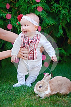 Cute funny happy baby with rabbit making his first steps on a green grass