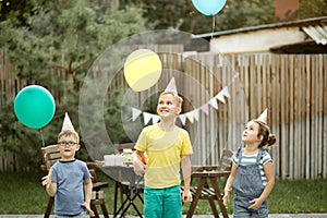 Cute funny kids celebrating birthday with family or friends in a backyard. Birthday party. Kid wearing party hat and launch