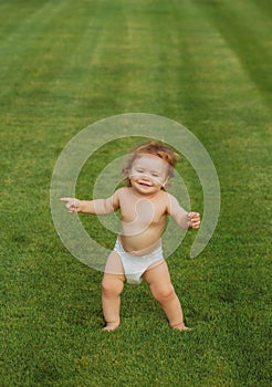 Cute funny laughing baby learning to crawl, having fun playing on the lawn watching summer in the garden. Little fun