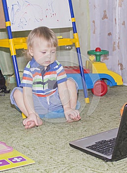 Cute funny little baby boy with long blonde curly hair playing on computer and mobile phone
