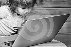 Cute funny little baby boy playing on computer and mobile phone near toy building blocks indoors.