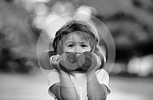 Cute funny little boy doing exercises with dumbbells in green park. Closeup portrait of sporty child with dumbbells