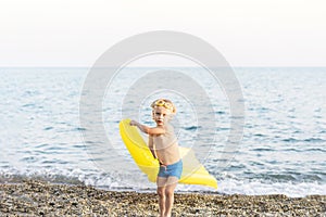 Cute funny little boy playing with yellow swimming mattress at sea shore. Summer beach vacation, childhood lifestyle