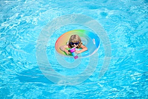 Cute funny little toddler boy in a colorful swimming suit and sunglasses relaxing with toy ring floating in a pool