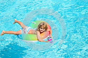 Cute funny little toddler boy in a colorful swimming suit and sunglasses relaxing with toy ring floating in a pool