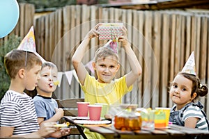 Cute funny nine year old boy celebrating his birthday with family or friends in a backyard. Birthday party. Kid wearing party hat