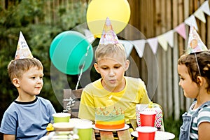 Cute funny nine year old boy celebrating his birthday with family or friends, blowing candles on homemade baked cake in a backyard