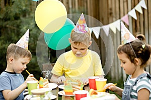 Cute funny nine year old boy celebrating his birthday with family or friends and eating homemade baked cake in a