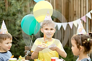 Cute funny nine year old boy celebrating his birthday with family or friends and eating homemade baked cake in a