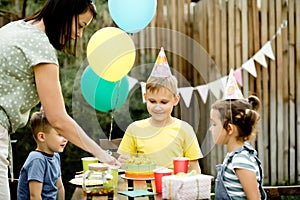 Cute funny nine year old boy celebrating his birthday with family or friends and eating homemade baked cake in a backyard.