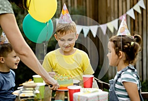 Cute funny nine year old boy celebrating his birthday with family or friends and eating homemade baked cake in a backyard.